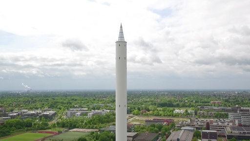 Der Bremer Fallturm sieht aus wie ein überdimensionaler Bleistift, der in den Himmel ragt. Im Hintergrund ist das Uni-Gelände zu sehen.