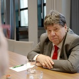 Ein Mann mit Perrücke und Anzug sitzt an einem Besprechungstisch.