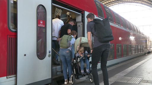 Eine familie hebt einen Kinderwagen mit einem Kleinkind in den Zug der Deutschen Bahn.