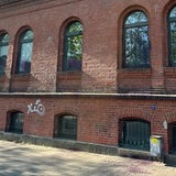 Eine rote Backsteinwand eines Hauses, die Fenster und der Boden davor sind mit lila Farbe beschmiert.