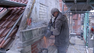 Ein Mann arbeitet mit einer Flex an einer Fassade.
