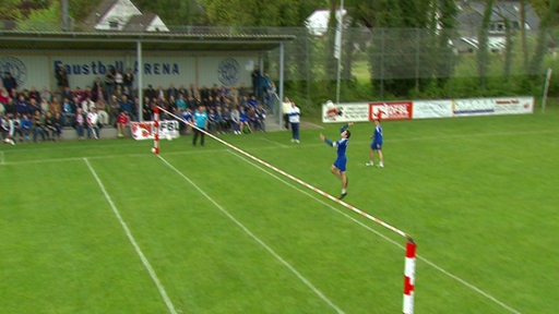 Menschen beim Faustballspiel im Stadion - die blaue Mannschaft schlägt den Ball gerade über die Markierungslinie in der Feldmitte