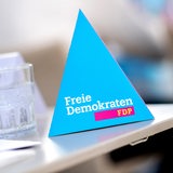 Ein Wasserglas steht auf einem Tisch, daneben ein dreieckiger Aufsteller mit der Aufschrift "Freie Demokraten – FDP".