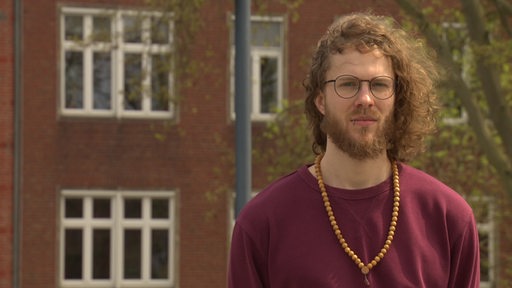 Felix Arndt, ein junger Mann mit Locken, steht vor dem Gebäude der Brebau an der Schlachte in Bremen.