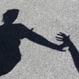 Ein Schattenbild auf dem Asphalt zeigt den Arm eines Mannes, der nach einer Frau greift. 
