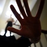 Im Treppenhaus macht eine Person eine abwehrende Handbewegung, während im Hintergrund eine Person auf dem Treppenabsatz steht.