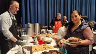 Mehrere Personen stehen vor und hinter einem Tisch mit Kuchen.