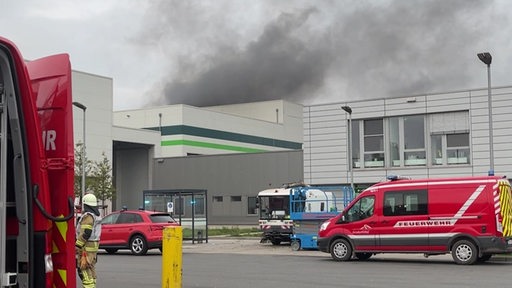 Große graue Brandwolken über der Sortieranlage in Bremen Nord, vor dem Gebäude stehen Feuerwehrautos. 
