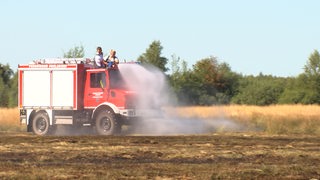 Ein Einsatzfahrzeug der Feuerwehr löscht ein Feld.