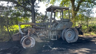 Ein ausgebrannter Traktor steht auf einem Weg.