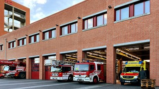 Ein Gebäude aus roten Backsteinen, die Feuer- und Rettungswache; mit Feuerwehrwagen davor.