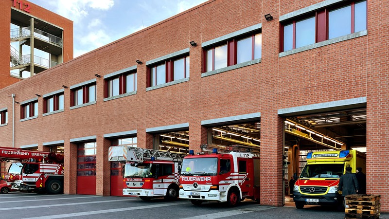 Ein Gebäude aus roten Backsteinen, die Feuer- und Rettungswache; mit Feuerwehrwagen davor.