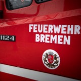 "Feuerwehr Bremen" steht auf der Tür eines Einsatzfahrzeuges. Im Hintergrund steht ein Feuerwehrmann.
