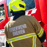 Ein Feuerwehrmann ist bei einer Übung der Feuerwehr Bremen von hinten zu sehen. Er steht vor einem Einsatzfahrzeug.