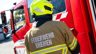 Ein Feuerwehrmann ist bei einer Übung der Feuerwehr Bremen von hinten zu sehen. Er steht vor einem Einsatzfahrzeug.