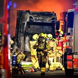 Feuerwehrleute stehen vor einem ausgebrannten Lastwagen. 