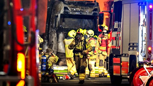 Feuerwehrleute stehen vor einem ausgebrannten Lastwagen. 