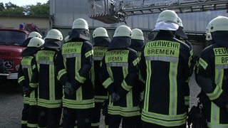 Mehrere Männer der Feuerwehr Bremen stehen mit dem Rücken zur Kamera.  