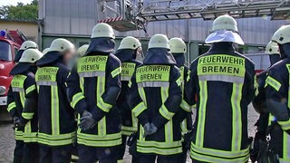 Mehrere Feuerwehrmänner sind von hinten in Dienstuniformen zu sehen.