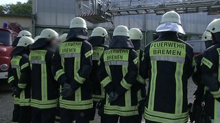 Personen der Feuerwehr Bremen, die dicht beieinander, mit dem Rücken zur Kamera stehen.