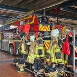In einer Halle stehen Feuerwehrautos  und Garderoben mit Uniformen.