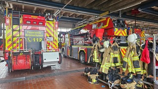 In einer Halle stehen Feuerwehrautos  und Garderoben mit Uniformen.