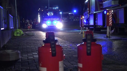 Zwei Feuerlöscher stehen vor einem Einsatzbereich der Feuerwehr im Bremer Stadtteil Gröpelingen.Im Hintergrund Einsatzfahrzeuge der Feuerwehr mit Blaulicht.