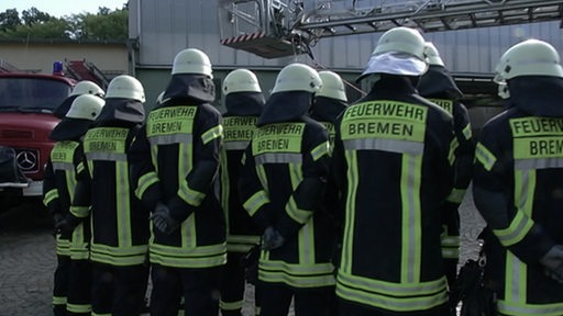 Zu sehen ist ein Gruppe von Feuerwehrleuten von hinten.