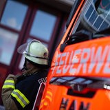 Eine Einsatzkraft der Feuerwehr steht während eines Pressetermins neben einem Einsatzfahrzeug der Feuerwehr.