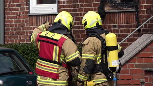 Zwei Feuerwehrleute in Brandschutzmontur, einer trägt einen Sauerstofftank auf dem Rücken