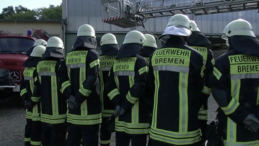 Eine Gruppe von Feuerwehrleuten in Arbeitskleidung von hinten.