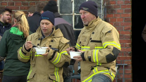 Zwei Feuerwehrmänner, die Suppe essen.