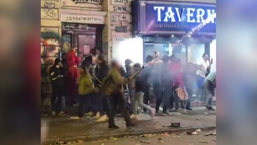 Eine Person sprüht im Bremer Viertel wahrlos mit Pyro in die Luft. Unbeteiligte Personen stehen um ihn herum.
