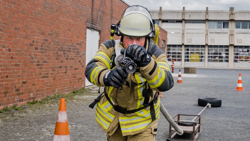 Ein Feuerwehrmann läuft mit einem Löschschlauch auf die Kamera zu 