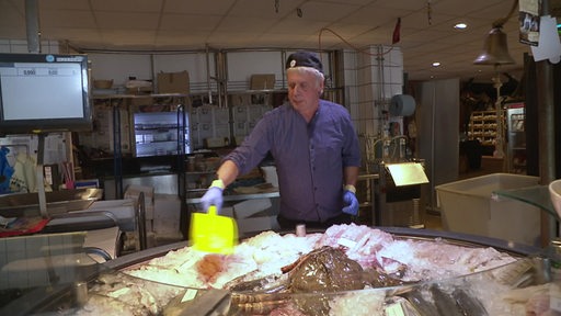 Ein Angestellter im Kühlhaus in der Fischerreihalle in Bremerhaven bestreut den ausgelegten, frischen Fisch mit Eis.