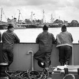 Historisches Schwarzweißbild. Vier Fischer blicken auf Boote im Fischereihafen Bremerhaven.