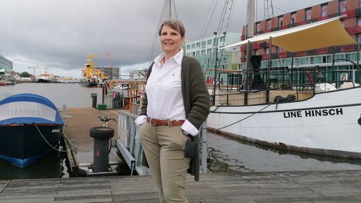 Eine Frau steht vor dem Hafenbecken im Bremerhavener Fischereihafen. Hinter ihr das Schiff "Line Hinsch".