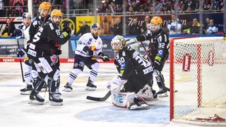 Die Eishockey-Spieler der Fischtown Pinguins und vom EHC München blicken dem Puck hinterher.