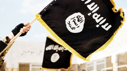 Hand hält Fahne der Terrororganisation Islamischer Staat