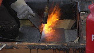 Eine Dachmatte wird von einem Handwerker flambiert und geschmolzen zum Festkleben. 