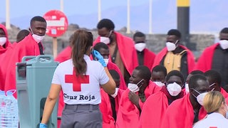Mehrere Geflüchtete sind in Decken gehüllt, eine Mitarbeiterin vom Roten Kreuz geht auf sie zu