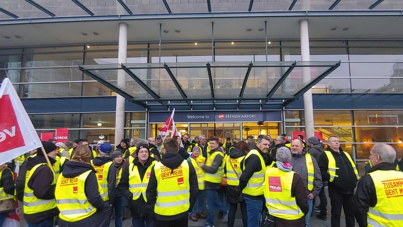 Beschäftigte des Öffentlichen Dienstes streiken in gelben Warnwesten vor dem Bremer Flughafen.