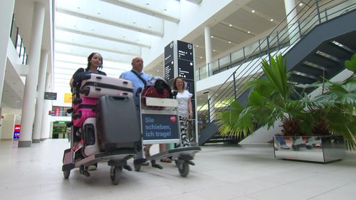 Eine Familie fährt mit zwei Gepäckwagen durch den Bremer Flughafen.