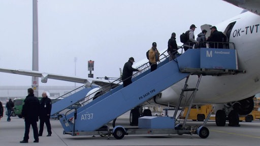 Zu sehen sind mehrere Fluechtlinge, die in ein Flugzeug einsteigen.