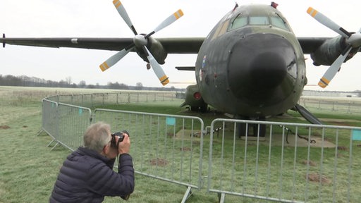 Zu sehen ist ein Mann, welcher ein Flugzeug fotografiert.