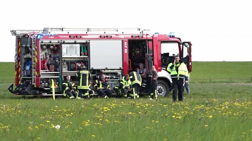 Ein Feuerwehrfahrzeug mit Besatzung auf einer Wiese.