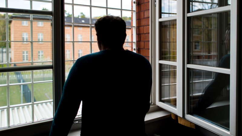 Ein Straftäter steht vor einem vergitterten Fenster in einer Klinik für Forensische Psychiatrie 