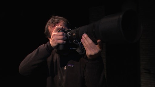 Der Journalist Andre Aden hält eine Kamera mit einem sehr großen Tele-Objektiv in den Händen.