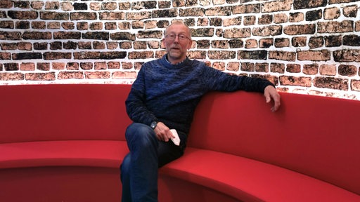 Ein Mann sitzt auf einem roten Sofa.