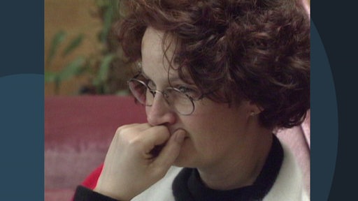 Eine Frau guckt kritisch über ihre Brille. Sie hat die Hand stützend vor ihrem Kinn.